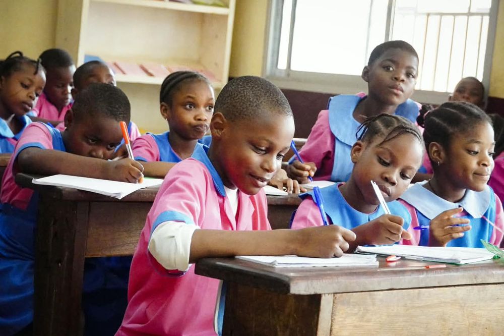 Primary pupils in pink and blue uniforms writing at their desks